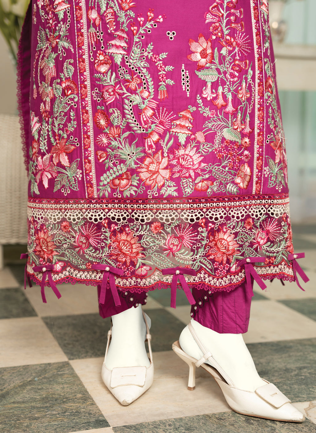 Traditional pink and red embroidered outfit with white shoes on a checkered floor.