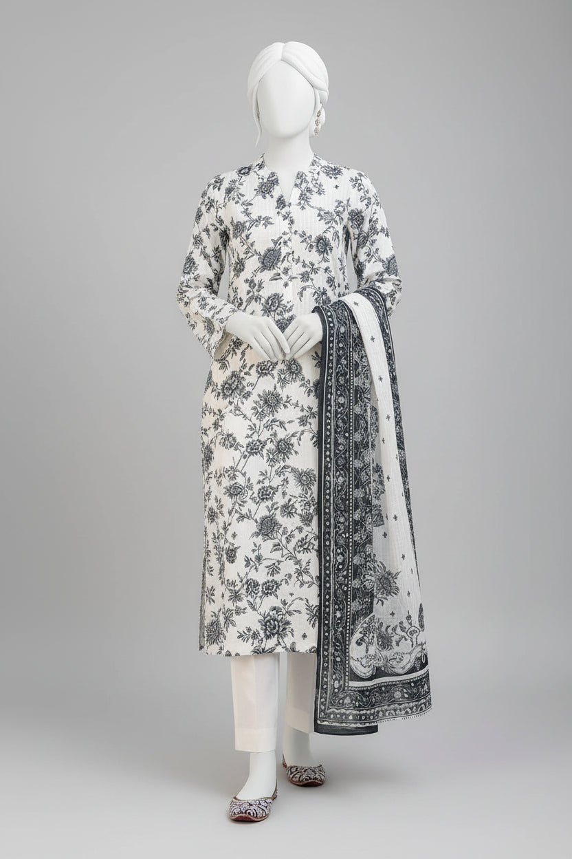 A three-piece women's salwar kameez suit set displayed on a mannequin in an outdoor courtyard. The set features an off-white/cream base with black floral and paisley block prints, including a long kurta, matching trousers, and a dupatta with ornate borders.