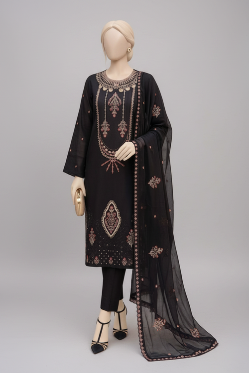 A black three-piece traditional outfit displayed on mannequins in an ornate indoor setting with gold-framed furniture, red cushions, and decorative orange flower arrangements. One mannequin stands upright showing the full kurta, pants, and dupatta, while the other sits to show the draped fabric detail.