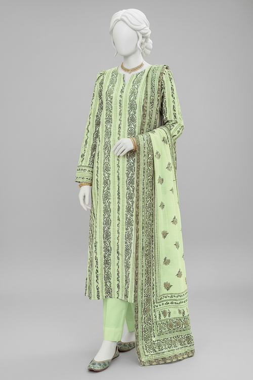 A light green traditional three-piece salwar kameez suit displayed on a mannequin in an outdoor garden setting decorated with flowers and a floral bench.