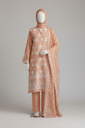Woman wearing a peach-colored traditional outfit with a matching headscarf in a warm-toned setting.