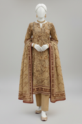 A traditional South Asian women's three-piece suit displayed on a mannequin in an outdoor garden setting. The set includes a heavily embroidered beige kurta with gold and brown floral patterns, matching beige trousers, and a coordinating dupatta with a brown border.