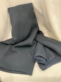A folded slate blue-gray knit fabric scarf or shawl with visible stitched edges, draped on a soft white fabric background.