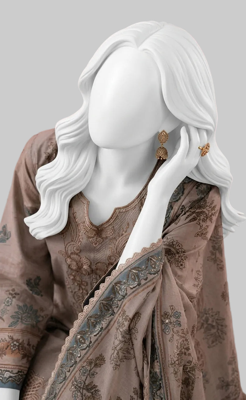 A white female mannequin wearing a brown embroidered traditional outfit with a patterned dupatta and gold earrings, set against a soft pink background.