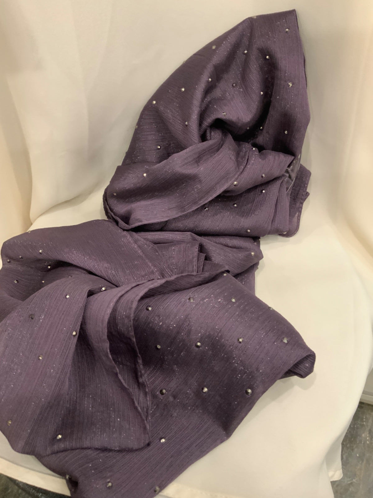 A draped piece of textured purple fabric with small scattered silver rhinestone accents, displayed on a white draped chair.