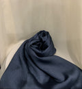 A dark navy blue textured fabric, likely a scarf or lightweight wrap, draped and rolled on a white draped studio backdrop.