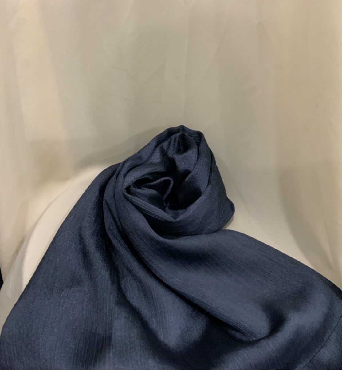 A dark navy blue textured fabric, likely a scarf or lightweight wrap, draped and rolled on a white draped studio backdrop.