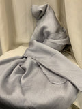 A light gray textured fabric, likely a silk scarf or throw, draped elegantly over a cream-colored chair against a matching draped fabric backdrop.