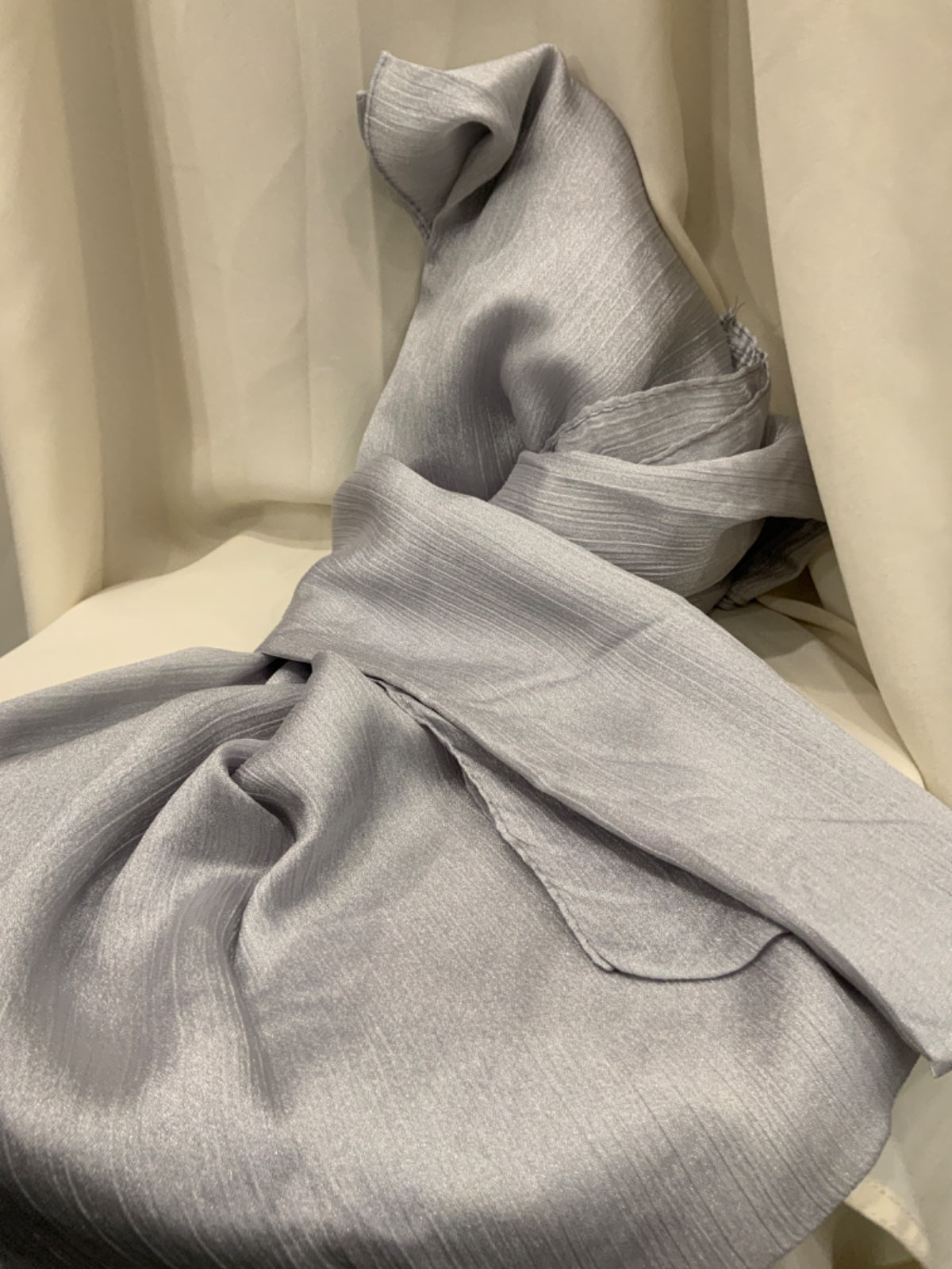 A light gray textured fabric, likely a silk scarf or throw, draped elegantly over a cream-colored chair against a matching draped fabric backdrop.
